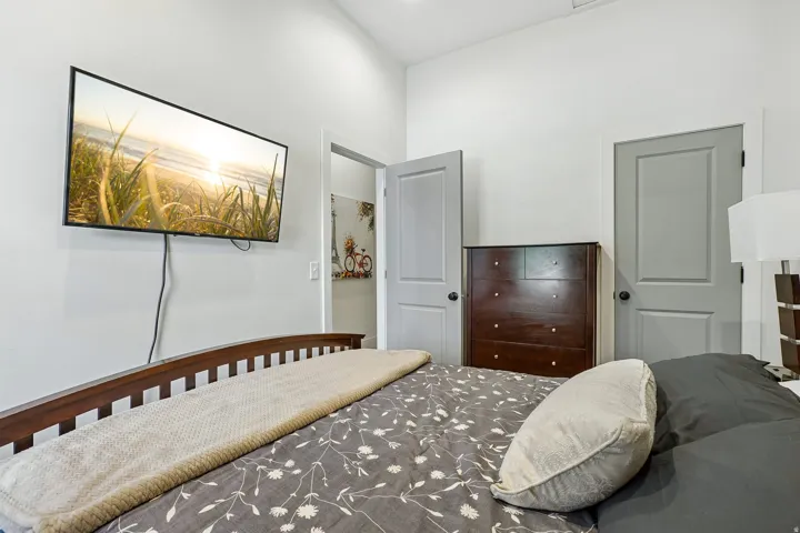 Bright secondary bedroom featuring warm wood-finish flooring, a wood-frame bed, dark wood dresser with multiple drawers, and dual gray-painted doors providing access to adjoining spaces