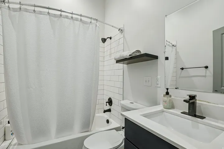 Bathtub with subway tile surround, dark bronze shower fixtures, floating vanity with white countertop, integrated sink, and wall-mounted mirror