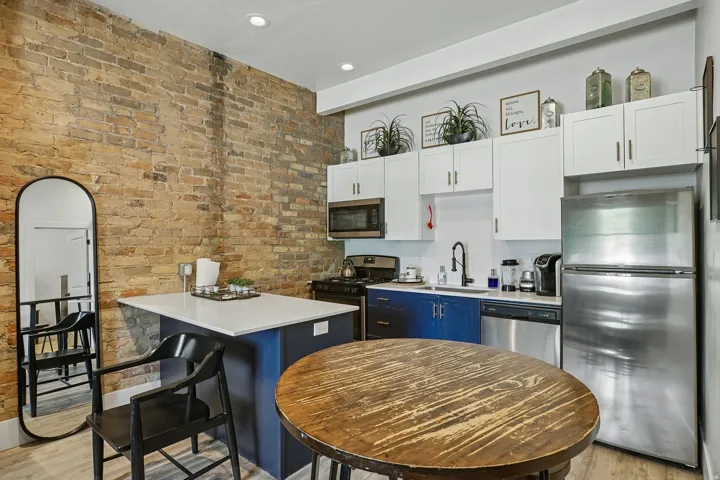 Modern kitchen featuring stainless steel appliances, including a double oven and refrigerator, complemented by white cabinetry with blue accent island