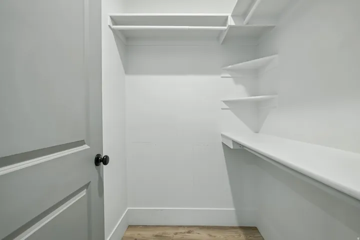 Spacious walk-in closet featuring custom white shelving and cabinetry, integrated LED lighting, and wood-finish flooring throughout