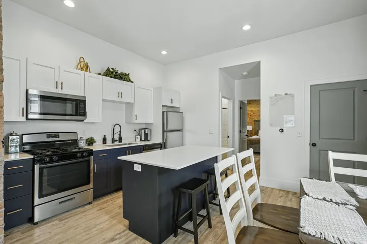 Modern kitchen featuring stainless steel appliances, including a gas range and built-in microwave, paired with white cabinetry and a dark blue kitchen island with seating