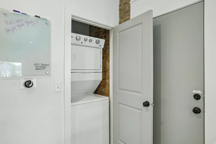 Dedicated laundry closet featuring a stackable washer and dryer unit with stainless steel controls, white cabinetry, and neutral finishes for convenient in-home clothing care