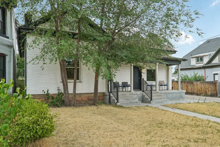 White brick facade with a covered front porch featuring round columns, black handrails, and a concrete walkway