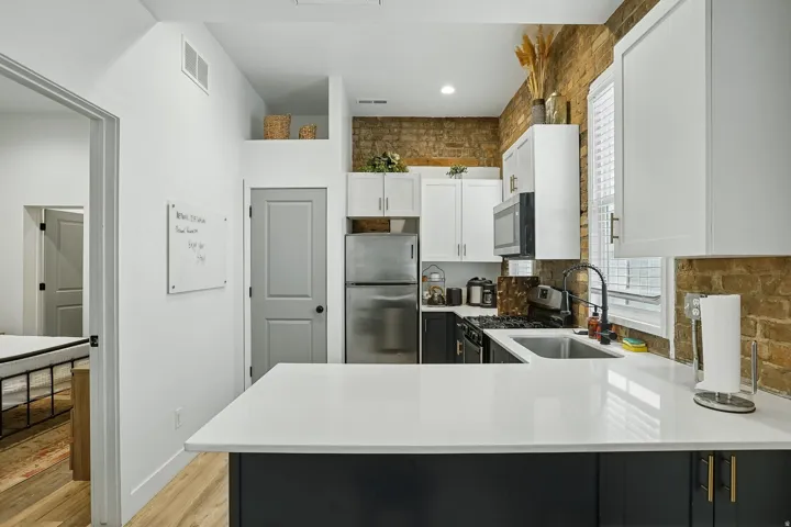 Modern kitchen featuring a two-tone cabinetry design with white upper cabinets and black lower cabinetry, white subway tile backsplash, stainless steel appliances, and a white quartz waterfall-edge island countertop