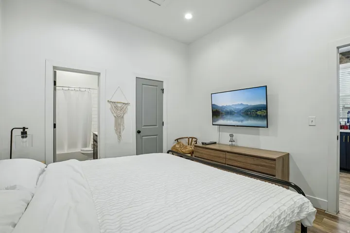 Serene primary bedroom with crisp white bedding, wood-finish flooring, and soft recessed lighting