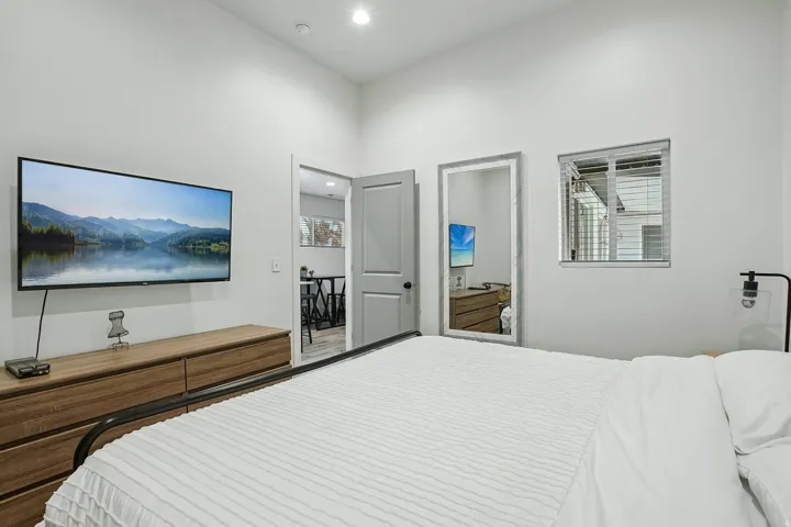 Modern primary bedroom featuring a wood-finish dresser with integrated storage, recessed ceiling lighting, and en-suite bathroom access