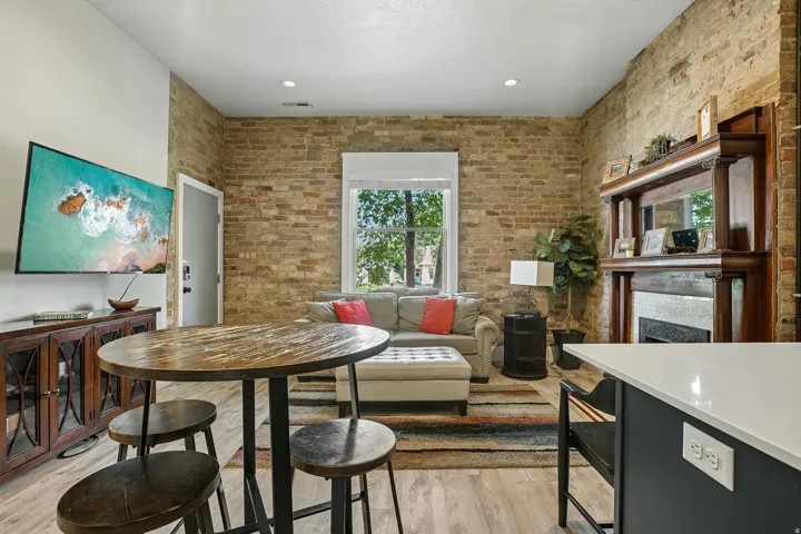 Open-concept living area featuring exposed brick walls, recessed ceiling lighting, and wood-finish flooring