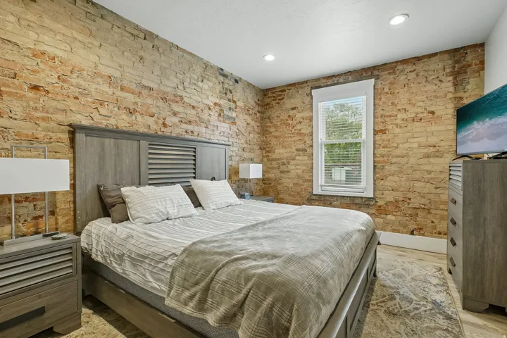 Exposed brick wall, recessed lighting, wood-finish flooring, and a window with blinds