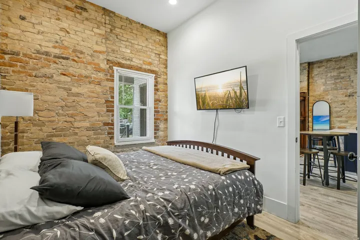 Bedroom featuring exposed brick accent wall, wood-finish flooring, and abundant natural light from large window