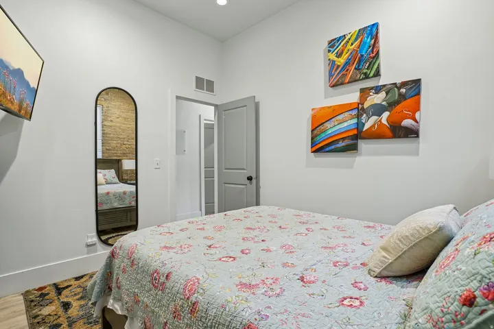 Bright secondary bedroom featuring wood-finish flooring, an arched mirror, and colorful abstract artwork
