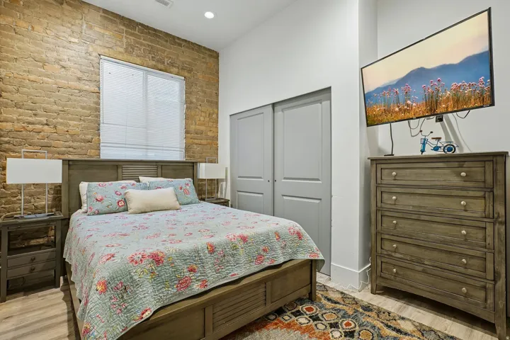Exposed brick accent wall, wood-finish flooring, recessed lighting, and a window with blinds