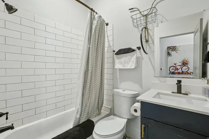 Modern bathroom featuring subway tile walls, a white porcelain vanity with integrated sink, quartz countertop, matte black faucet, and a bathtub with coordinating shower enclosure and neutral patterned curtain