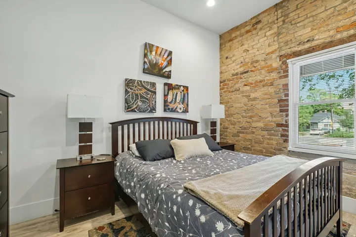 Exposed brick wall, recessed lighting, wood-finish flooring, and a large window with white blinds