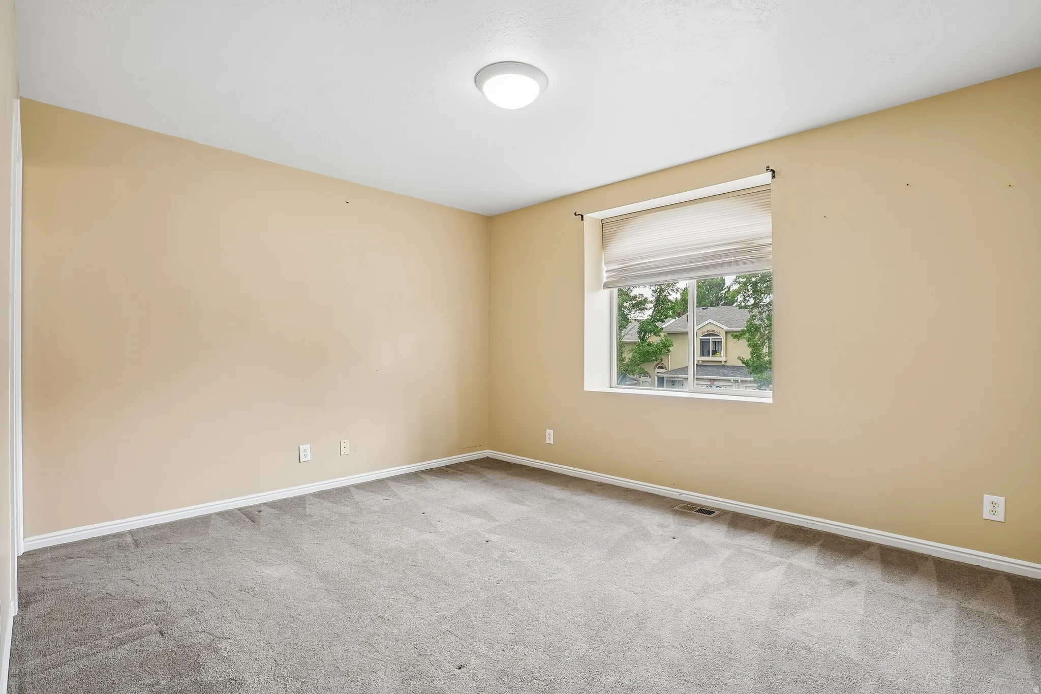 Carpeted room with a central window, featuring light beige wall paint and white trim