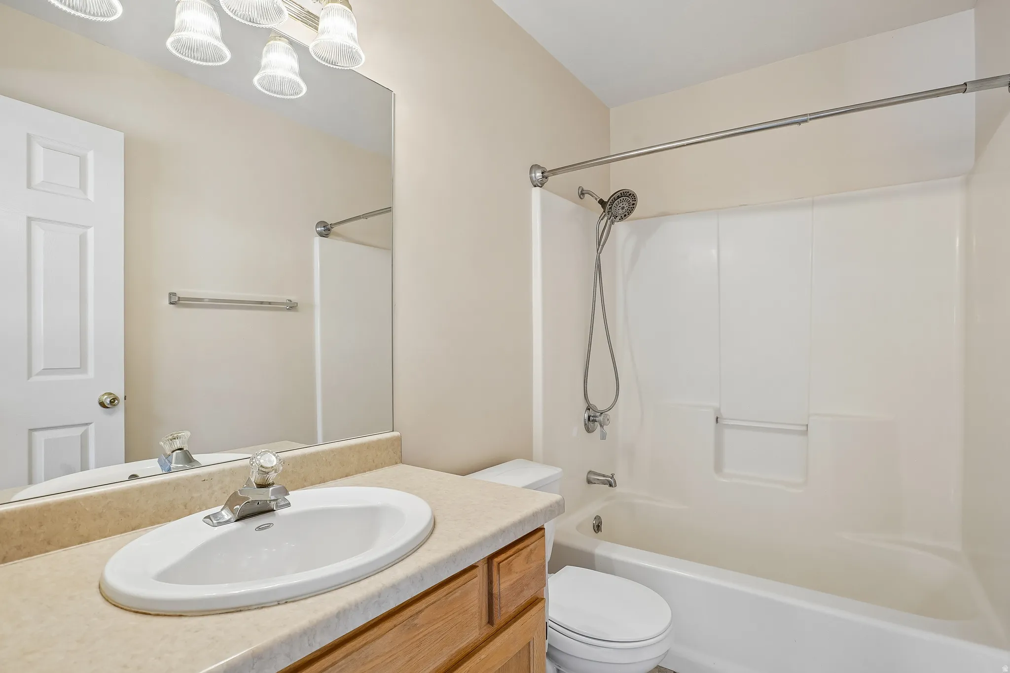 Bathroom featuring a wood-finish vanity with an integrated sink, a large wall-mounted mirror, and a full-size bathtub with a shower surround
