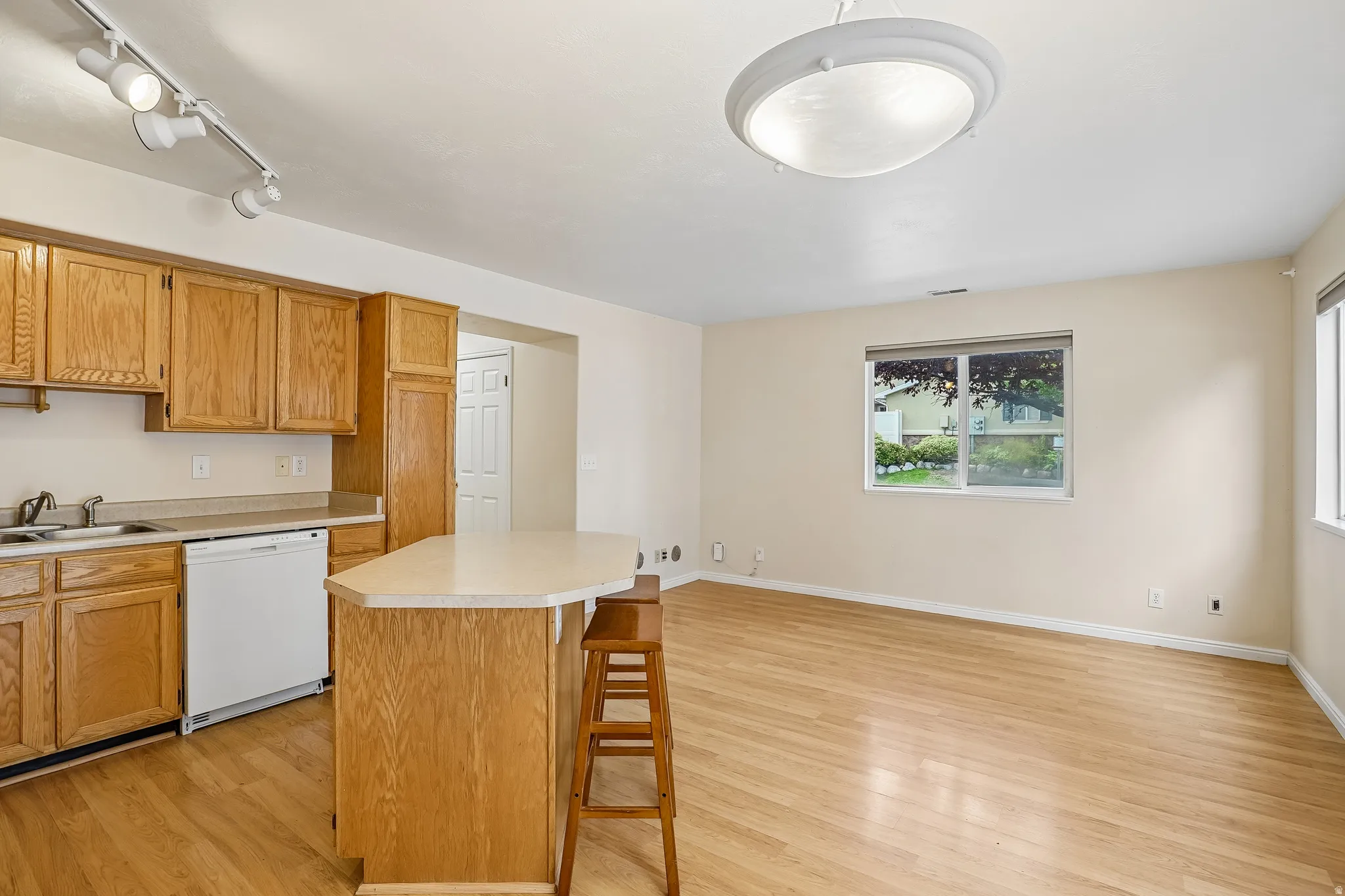 Open concept living area featuring wood-finish flooring, ample natural light, a kitchen island with countertop seating, and track lighting