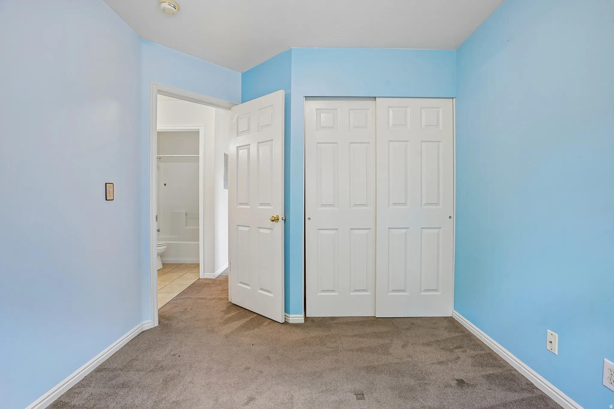 Bedroom featuring light blue walls, gray carpet, white trim, and a white bi-fold closet