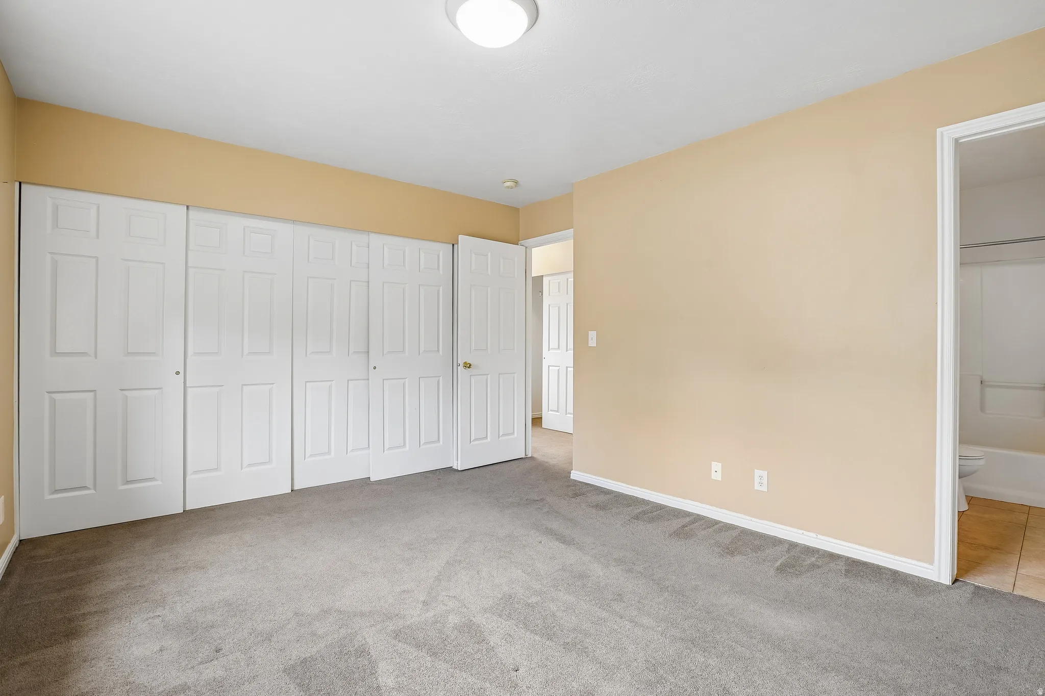 Spacious interior room featuring light beige walls and grey carpeting