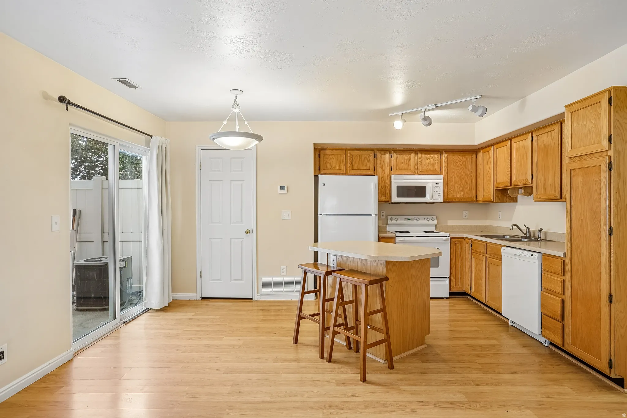 Kitchen featuring wood-finish flooring, light wood cabinetry, and white appliances
