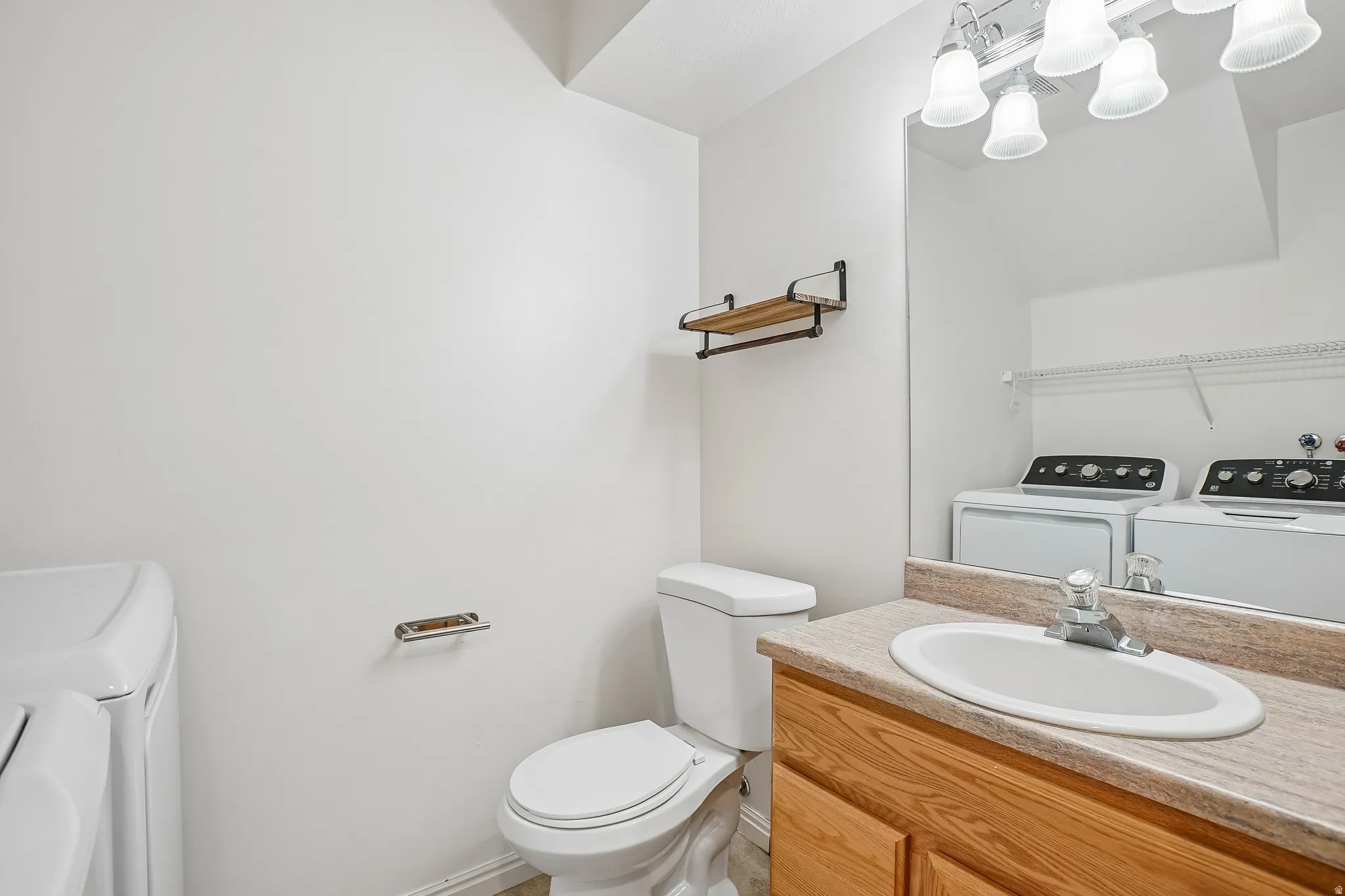 Powder room featuring a single vanity with wood-finish cabinetry, a large wall-mounted mirror, and a built-in toilet