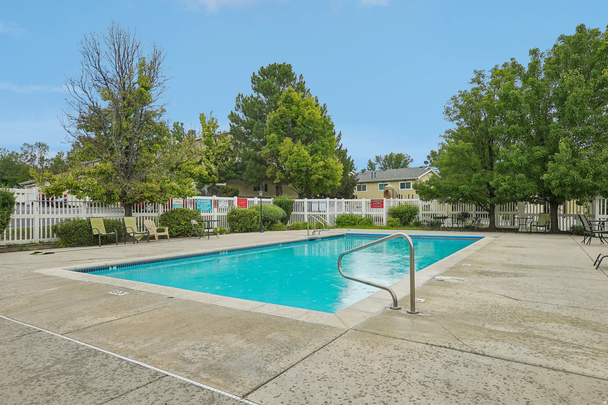 Rectangular swimming pool featuring a concrete surround, metal handrails, and a white picket fence perimeter