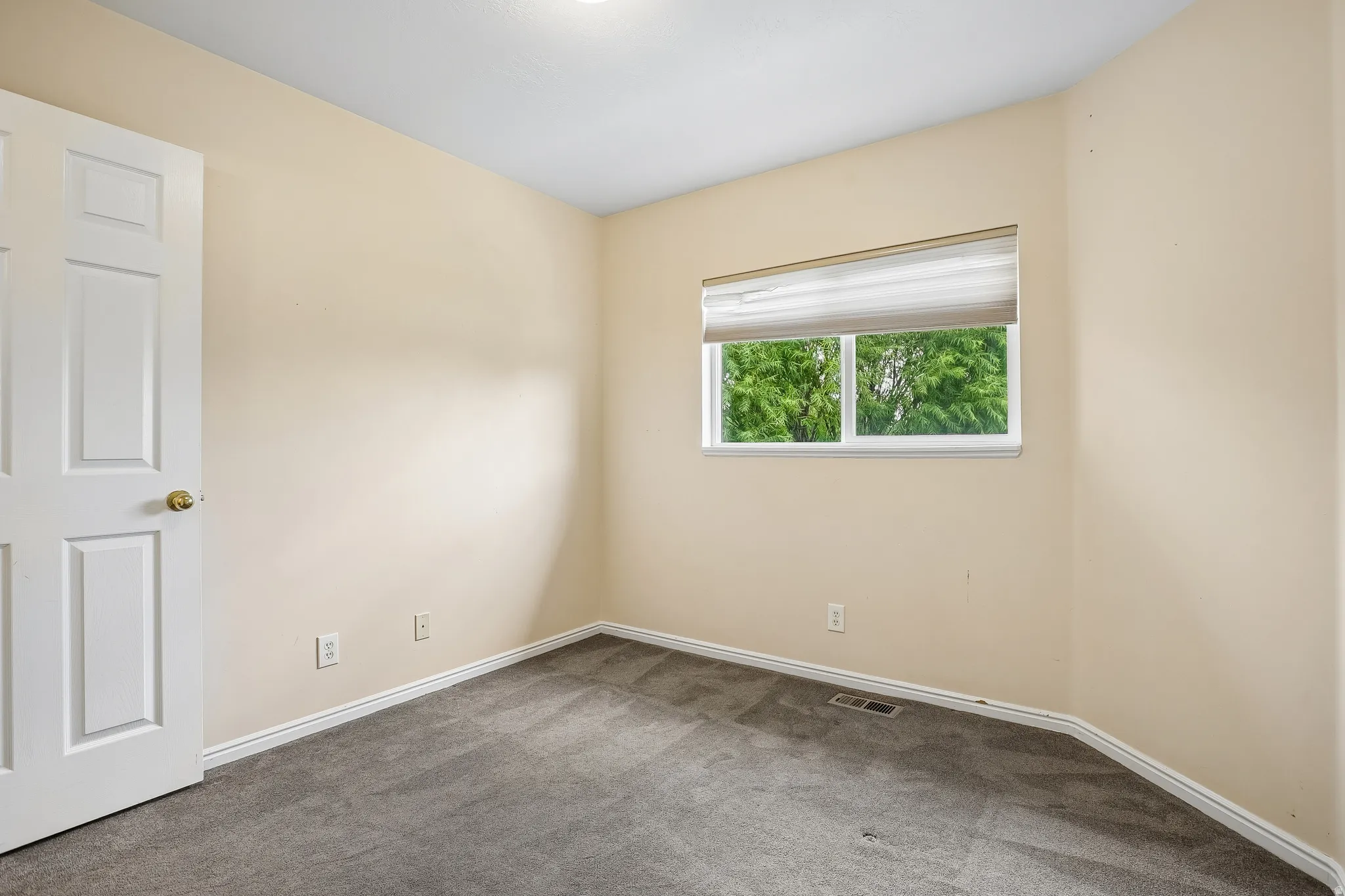 Neutral-toned room featuring a single window with blinds, light-colored walls, and gray carpeting