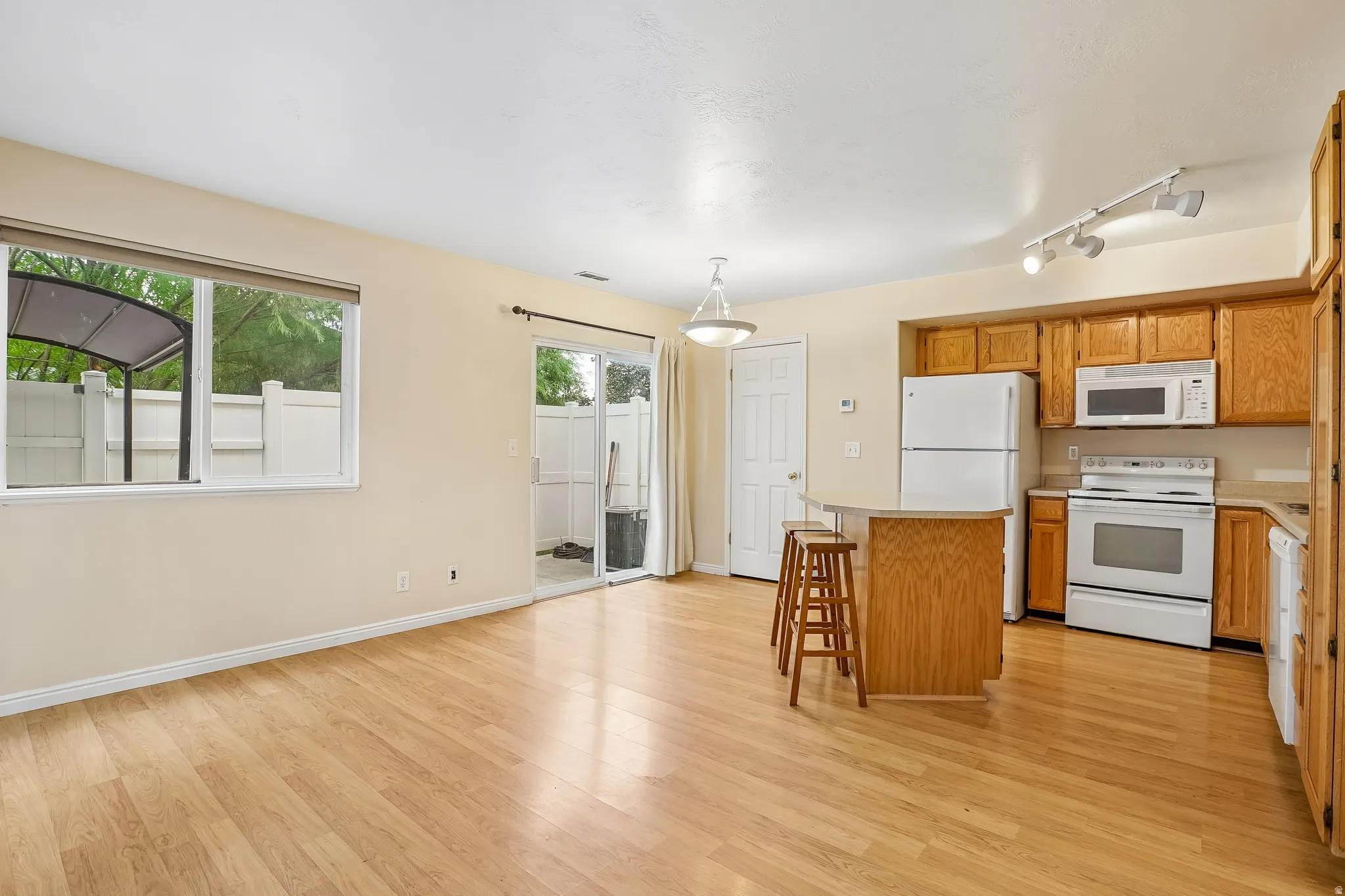 Open-concept living area featuring wood-finish flooring, a kitchen island with seating, and a sliding glass door leading to an outdoor patio