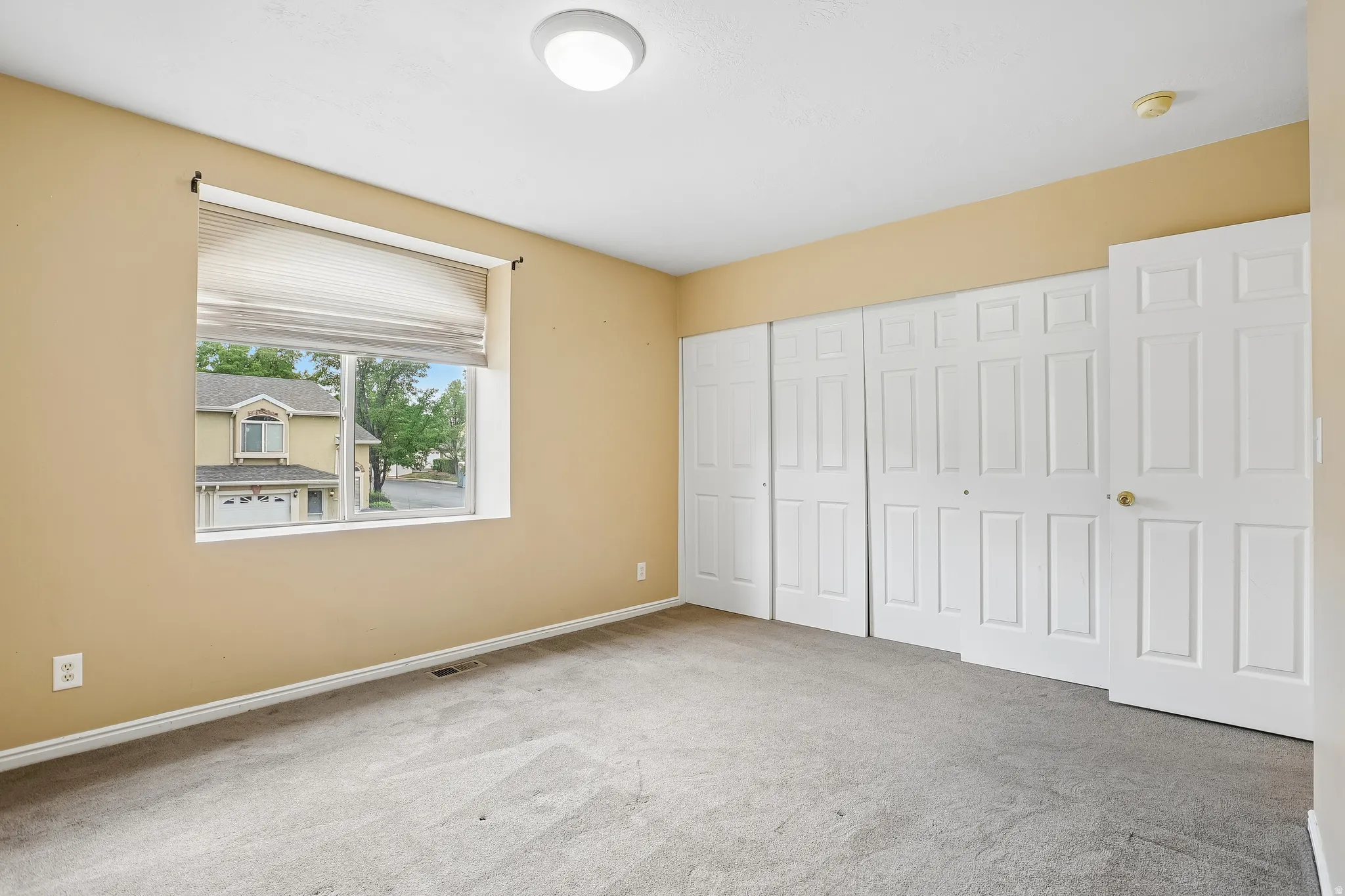 Carpeted room featuring neutral-toned walls, a single window with blinds, and multiple paneled doors