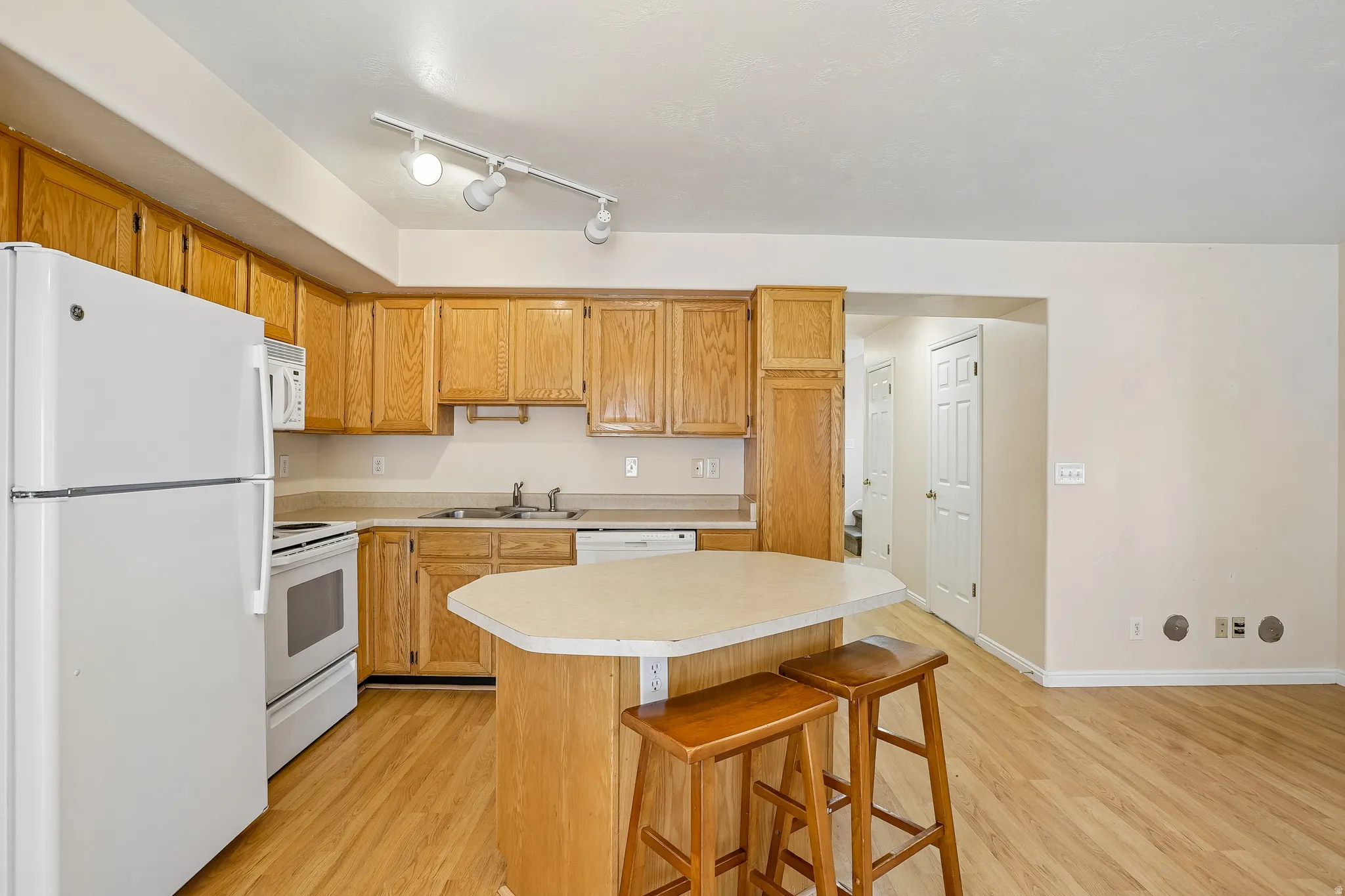 Kitchen featuring wood-finish flooring, a central island with a countertop, light wood cabinetry, and white appliances