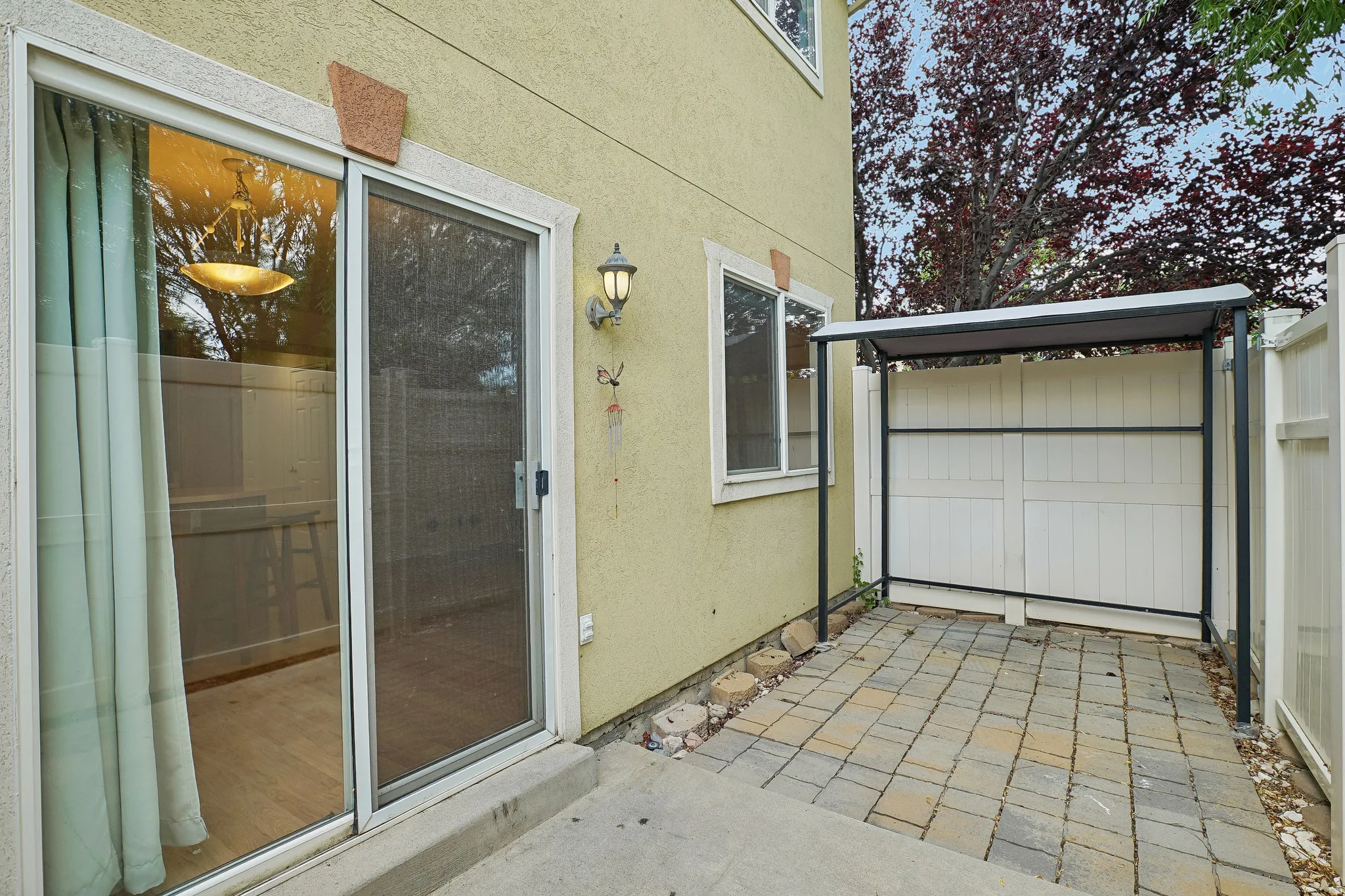 Private patio space featuring paver stone flooring, a metal-framed awning, and white privacy fencing