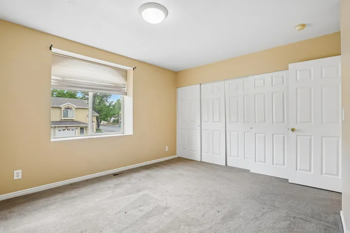 Carpeted room featuring neutral-toned walls, a single window with blinds, and multiple paneled doors