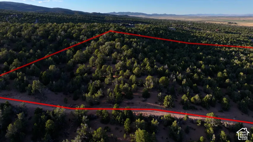Expansive lot featuring native juniper trees, rugged terrain, and mountain backdrop