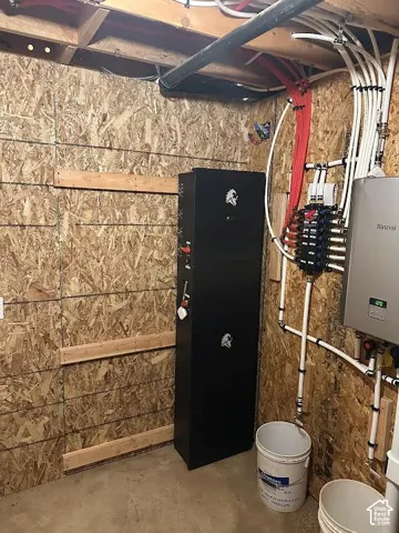 Utility room featuring a tankless water heater, water manifold system, exposed wood-finish walls, and a concrete floor