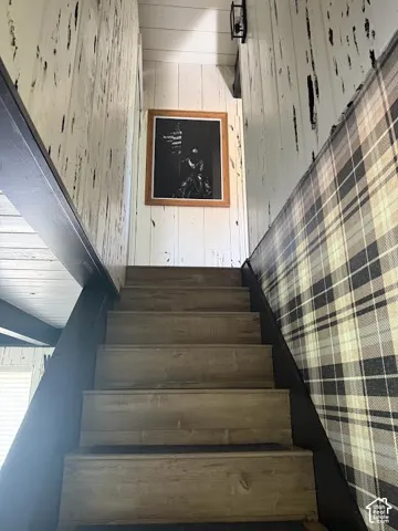 Stairway featuring wood-finish treads, a black newel post, and a wall adorned with plaid wallpaper