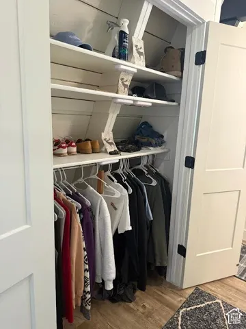 Recessed closet storage featuring white shelving, a hanging rod, and wood-finish flooring
