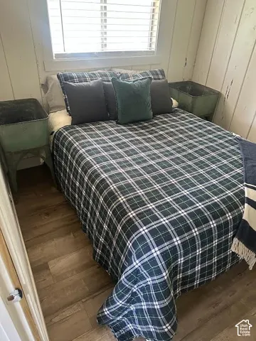 Bedroom featuring wood-finish flooring, a window with blinds, and white vertical plank walls