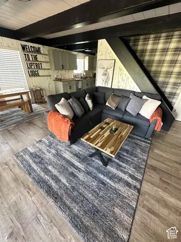 Open-concept living space featuring wood-finish flooring, exposed ceiling beams, and textured wall finishes