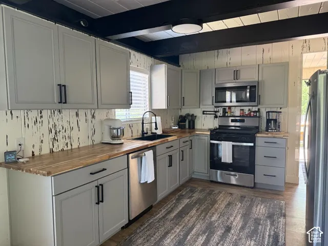 Contemporary kitchen featuring wood-finish countertops and light gray cabinetry with black hardware