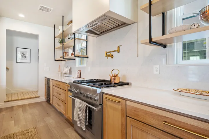 Modern kitchen featuring light wood cabinetry, white countertops, and a stainless steel range with matching hood