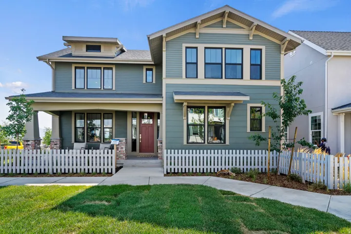 Craftsman-style home featuring a covered front porch with stone accents, a red front door, white picket fencing, and a dormer window