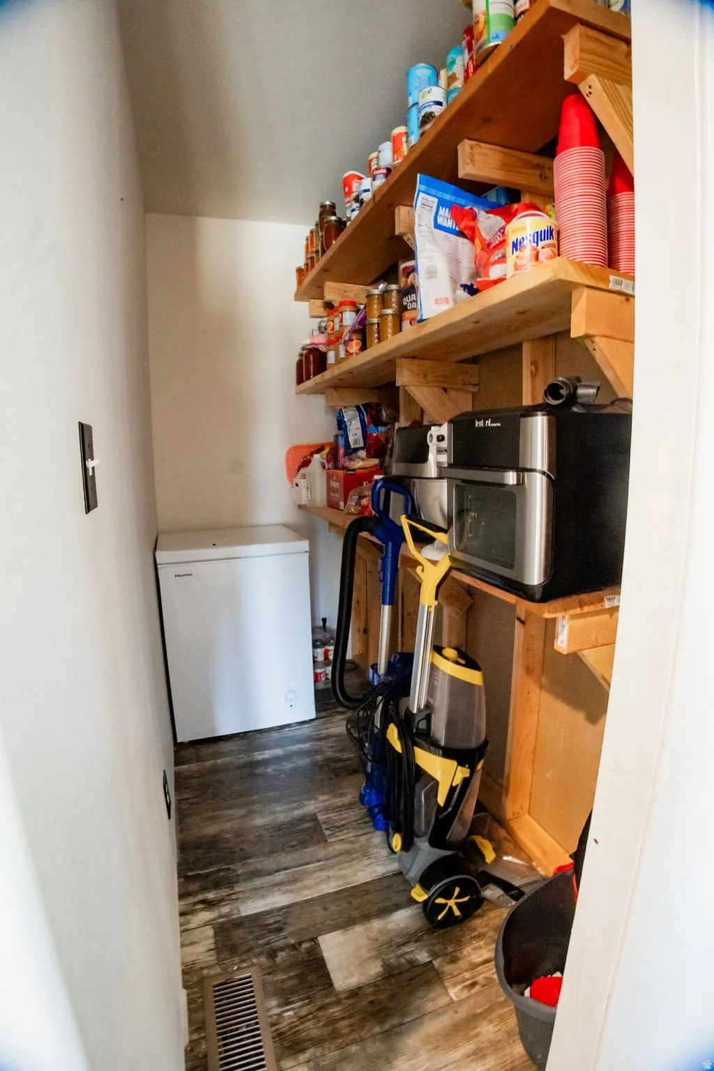Dedicated pantry space featuring built-in wooden shelving, wood-finish flooring, and a white chest freezer