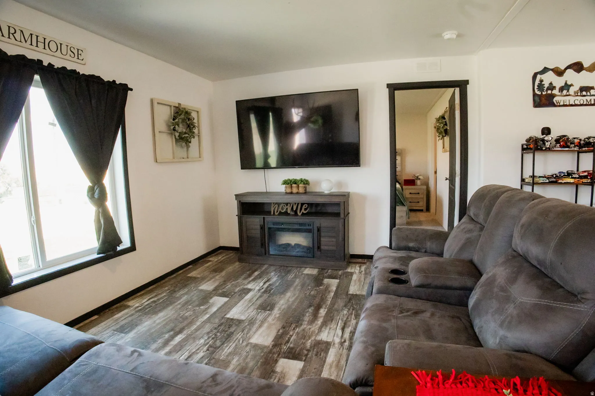 Living space featuring wood-finish flooring, white walls, and a large window with dark trim