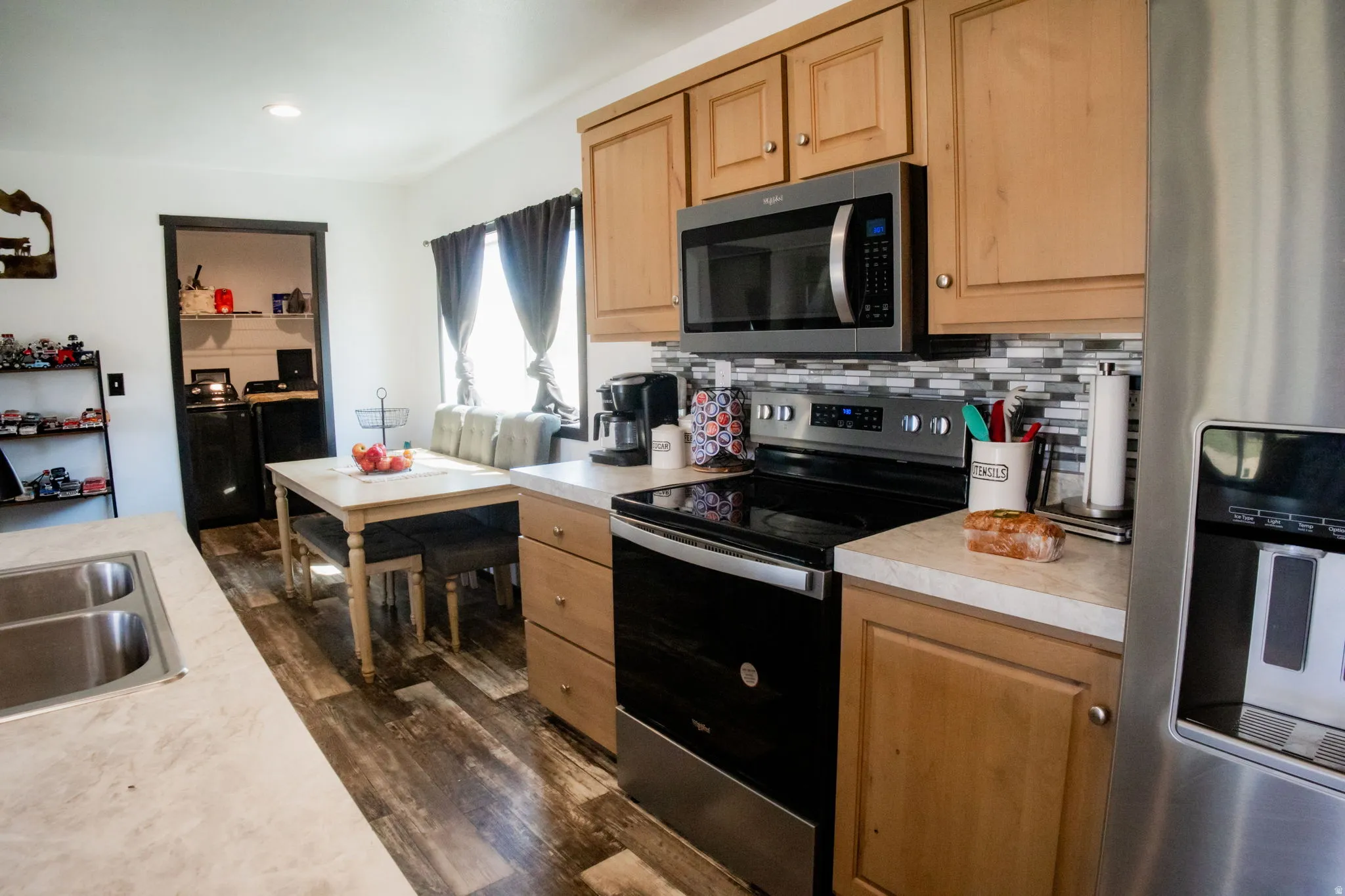 Kitchen featuring light wood cabinetry, stainless steel appliances, a tile backsplash, and light-toned countertops