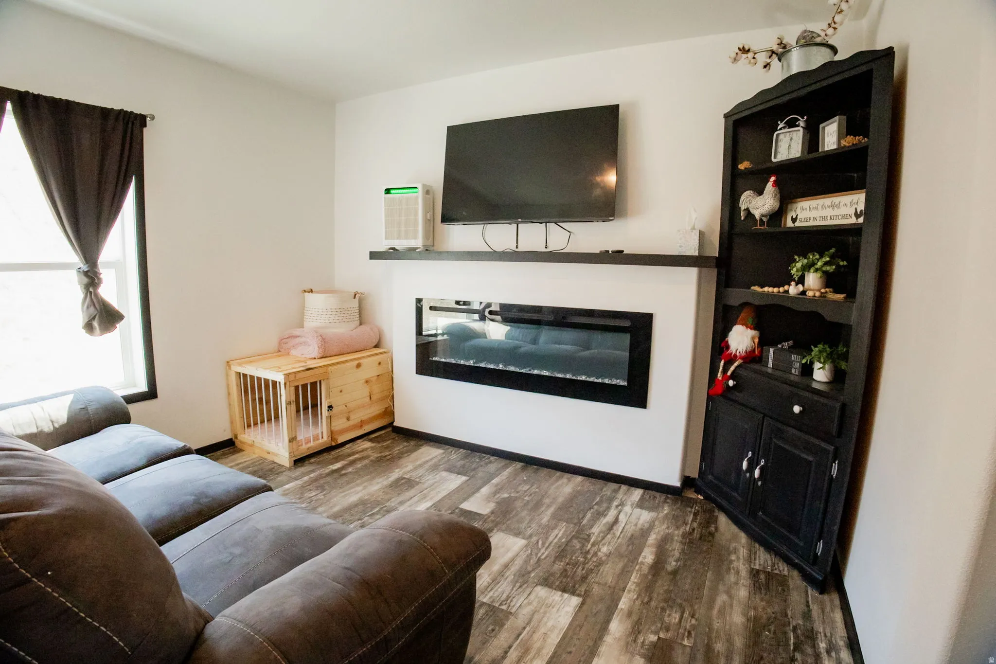 Living space featuring wood-finish flooring, an electric fireplace with a black mantel, and a dark corner hutch