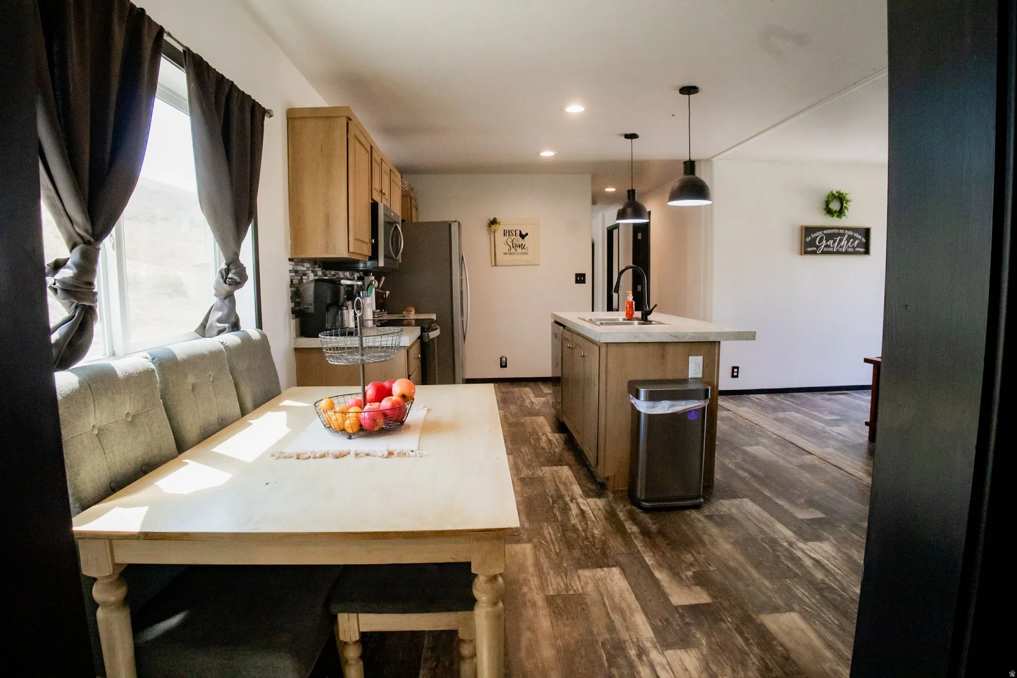 Open-concept kitchen and dining area featuring warm wood-finish flooring, a kitchen island with pendant lighting and integrated sink, stainless steel appliances, and light wood cabinetry