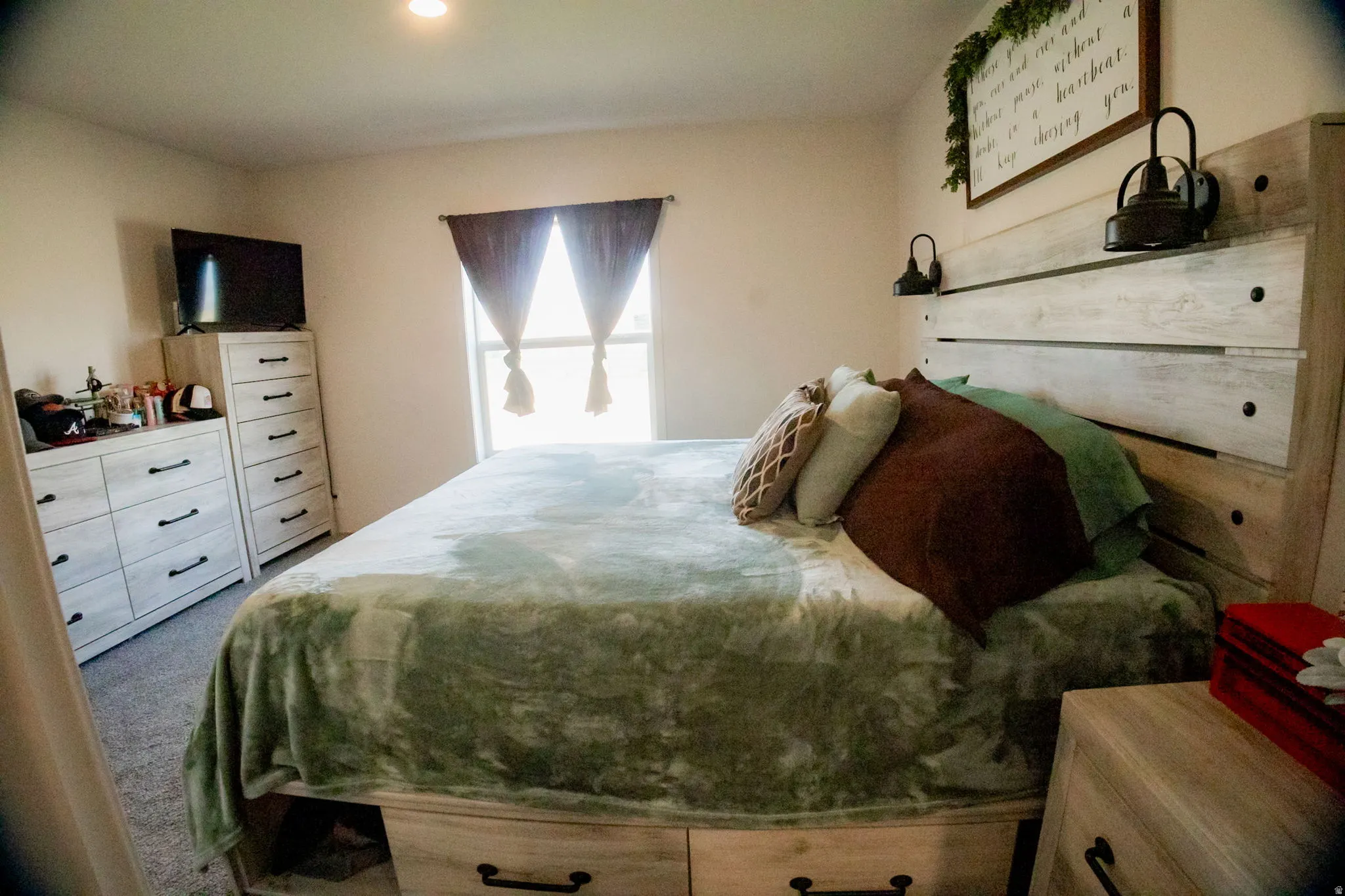Bedroom featuring a plank-style headboard with built-in wall sconces, soft carpet flooring, and a window with natural light