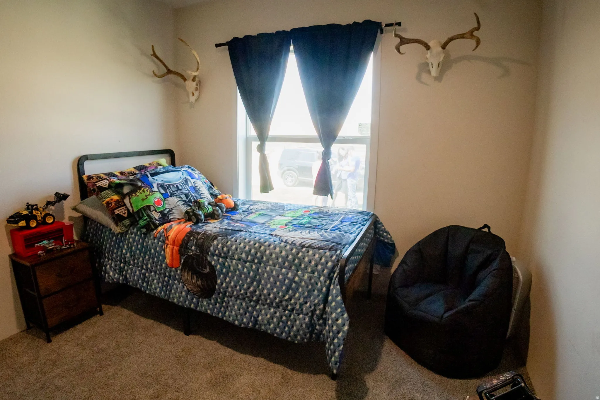 Carpeted room featuring a window with dark blue curtains, a dark wood-finish nightstand, and light-toned walls
