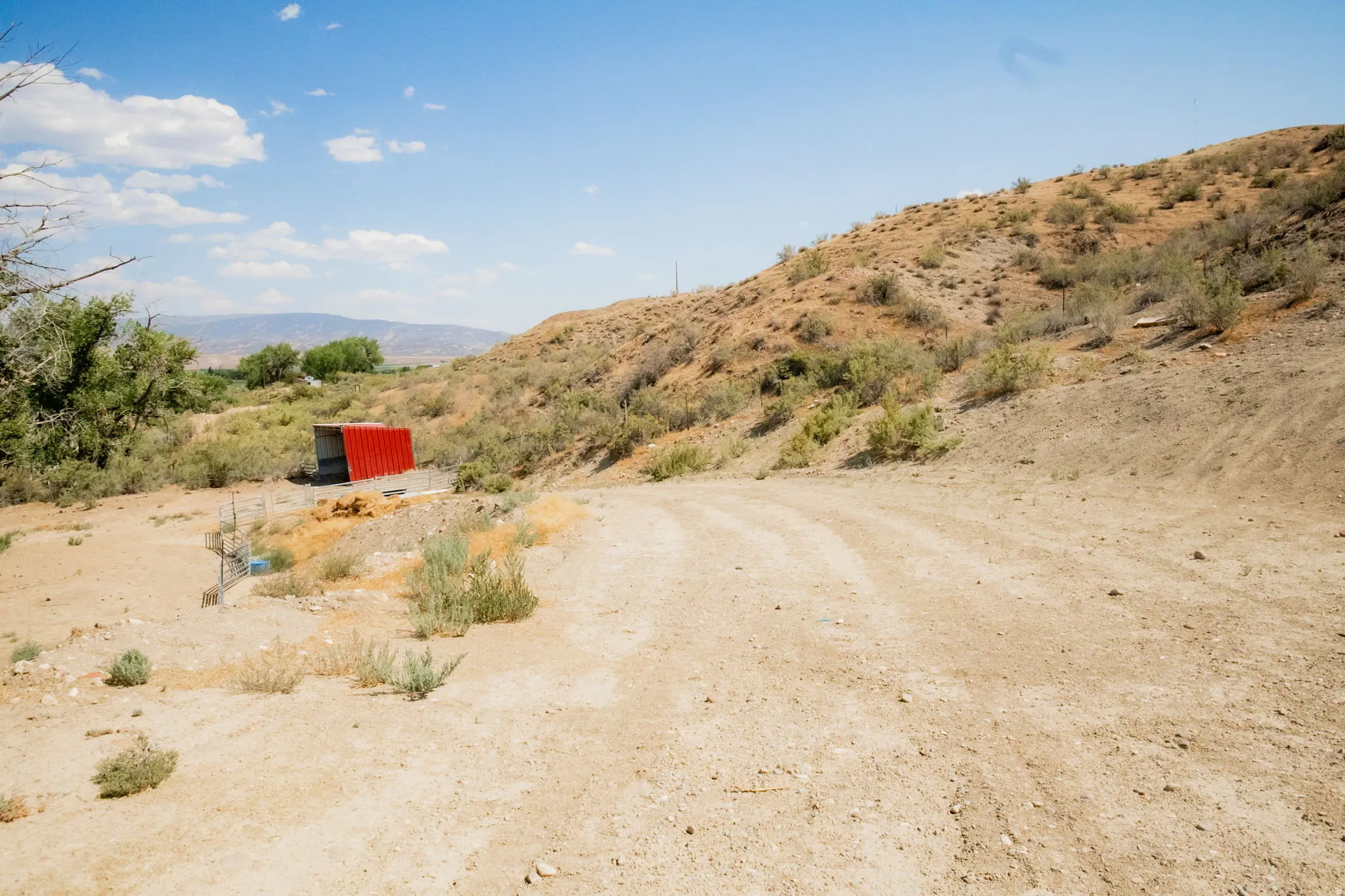 Expansive land parcel featuring a dirt road, natural terrain, and a vibrant red outbuilding