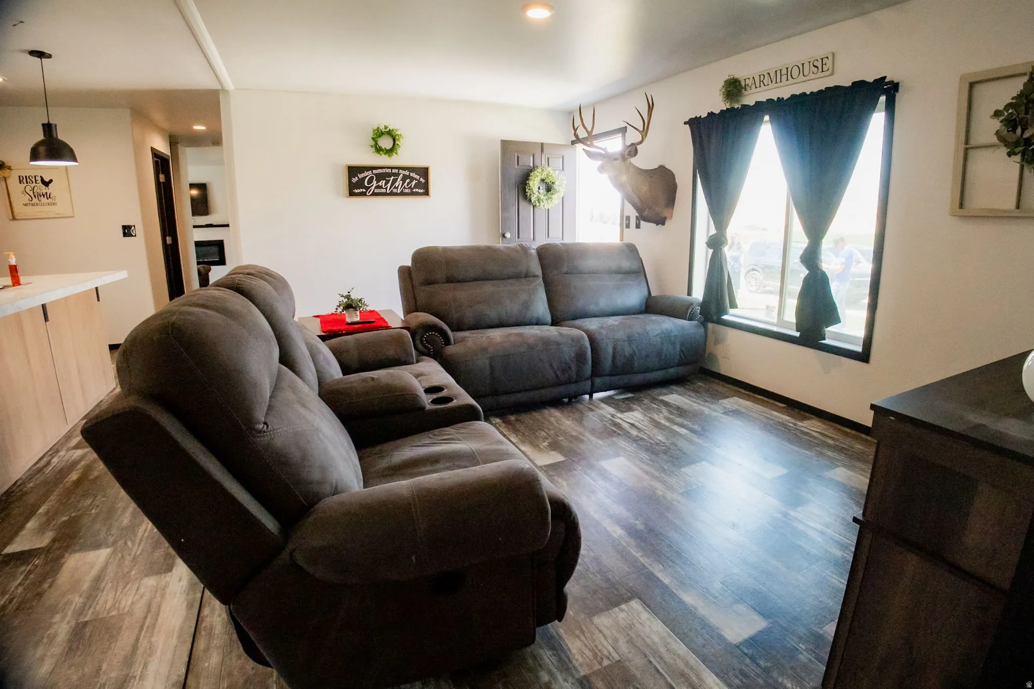 Spacious living area featuring wood-finish flooring, ample natural light from a large window, a built-in breakfast bar with a light-toned countertop, and a contemporary pendant light fixture