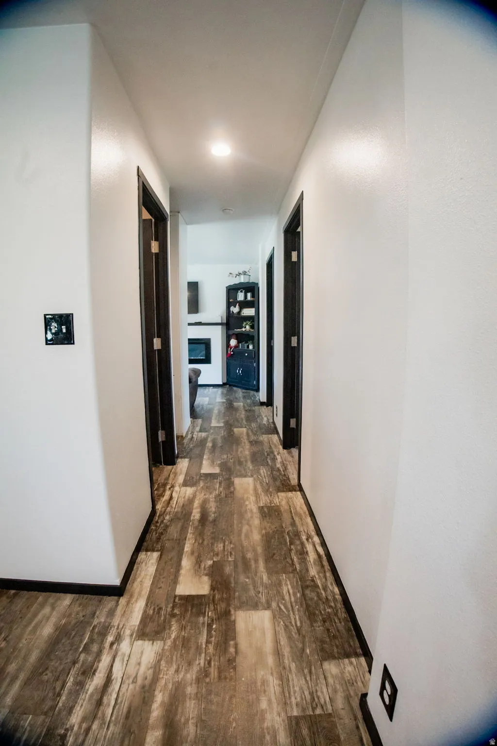 Hallway featuring wood-finish flooring, white walls, dark door frames, and recessed lighting